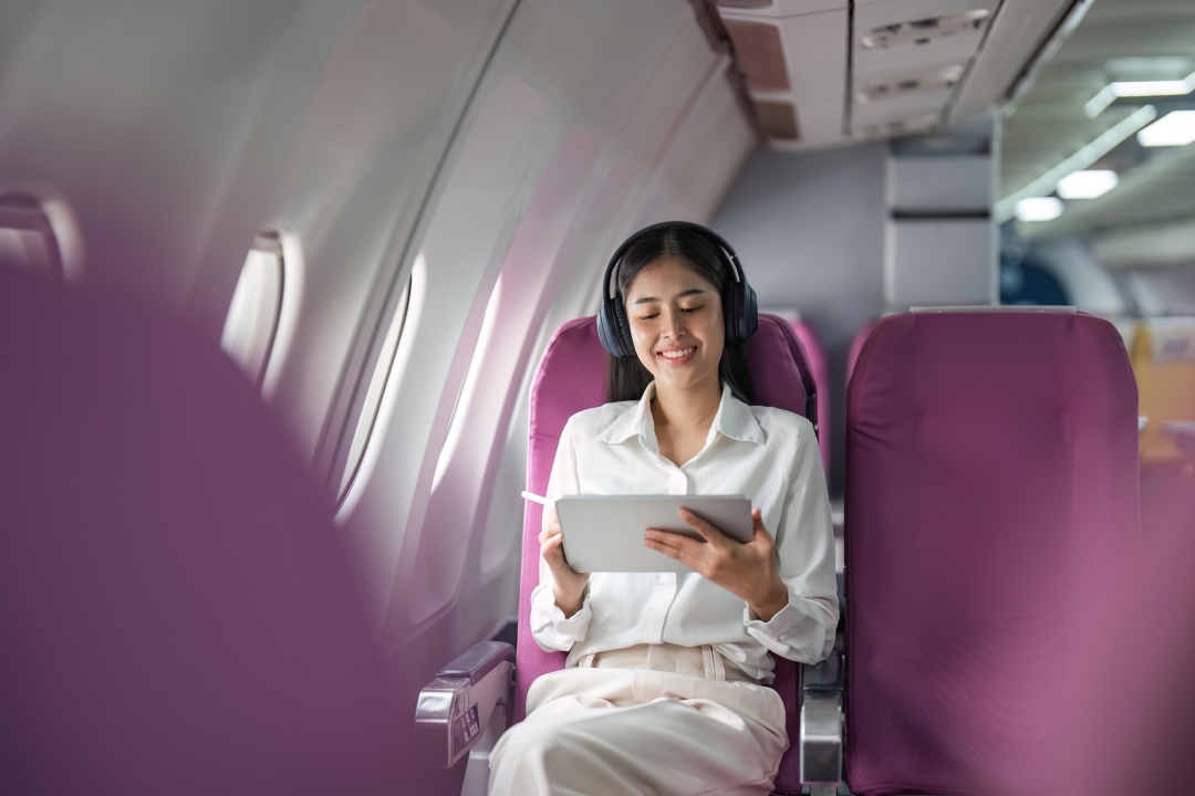 Chica viajando en avión con J1 Visa con audífonos y viendo su tablet.